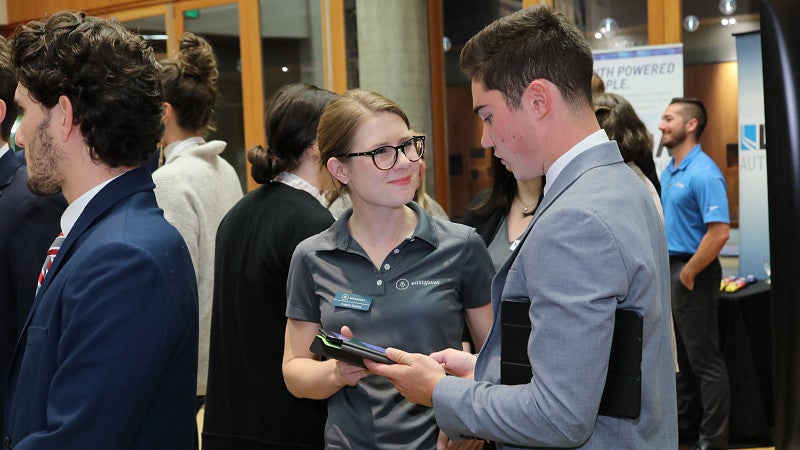 Student talking with industry professional, showing them an iPad at a networking event.