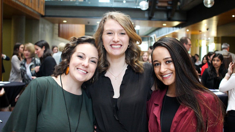 Group of three students standing together and smiling at the camera.