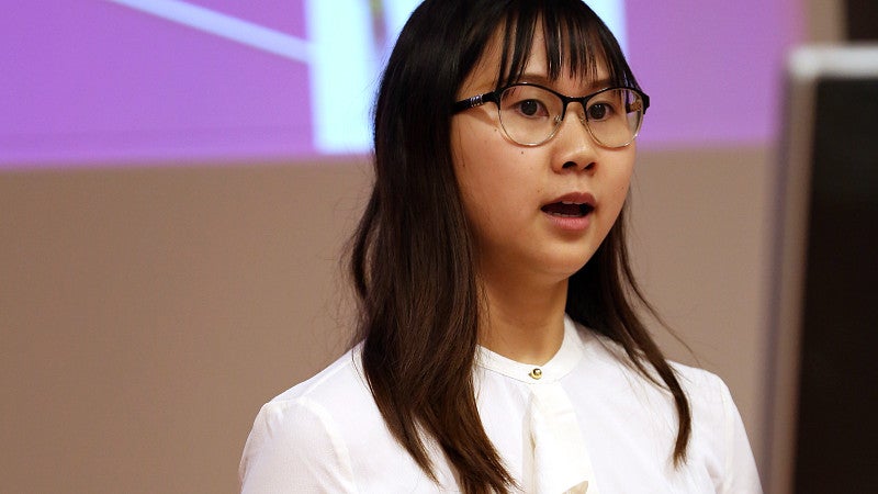 Close-up of one student standing with a presentation behind her talking to an audience