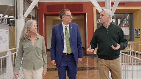 Sue Cameron McDonald (left) and Paul Cameron (right) walk through one of the upper stories of the atrium in the Lillis Business Complex, in conversation with University of Oregon president Karl Scholz (center).